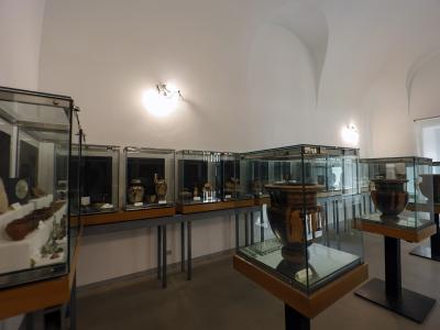 A museum gallery interior featuring glass display cases containing ancient pottery and artifacts, with white walls and arched ceilings.