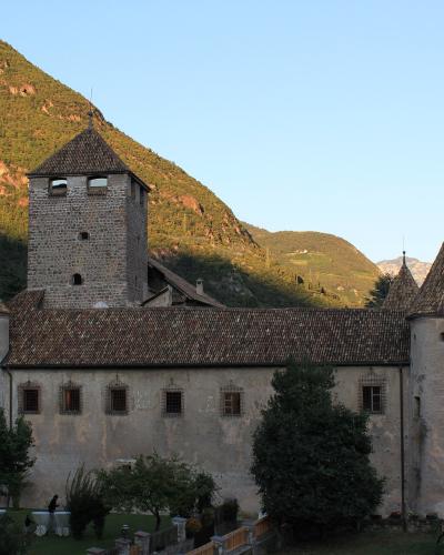 A stone castle with multiple conical-roofed towers and battlements, set against a clear blue sky with hills in the background; a blue recycling bin and wooden fence are visible in the foreground.