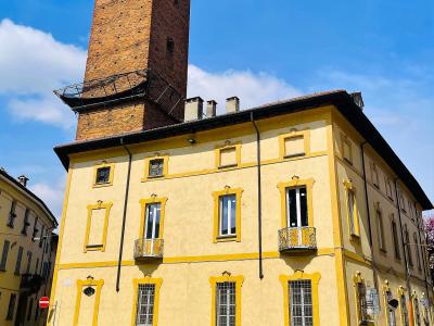 A tall, rectangular medieval brick tower rising behind a yellow-painted building with yellow-trimmed windows, situated on a cobblestone street under a blue sky.