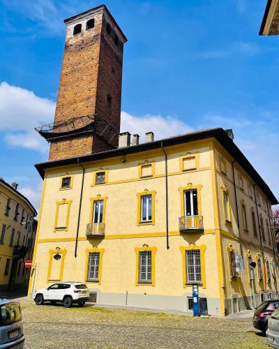 A tall, rectangular medieval brick tower rising behind a yellow-painted building with yellow-trimmed windows, situated on a cobblestone street under a blue sky.