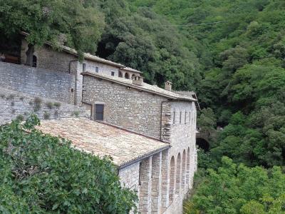 A stone Franciscan hermitage complex with terracotta-tiled roofs and arched loggias, nestled into a steep, densely forested hillside.