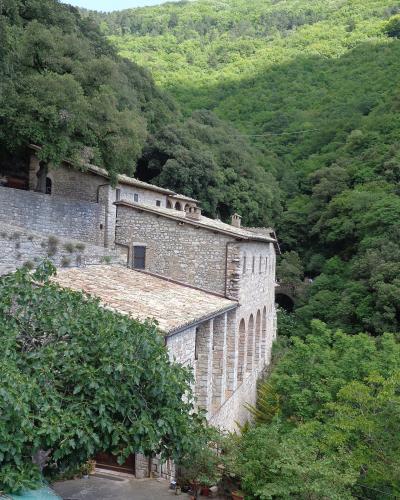 A stone Franciscan hermitage complex with terracotta-tiled roofs and arched loggias, nestled into a steep, densely forested hillside.
