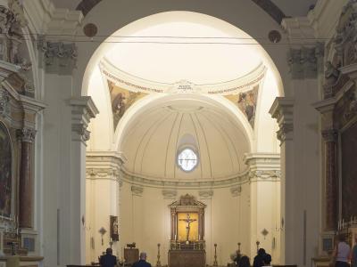 The image shows the interior of a church with a central nave, wooden pews, a domed apse, and an altar featuring a crucifix, with Latin inscriptions on the arch above the dome.
