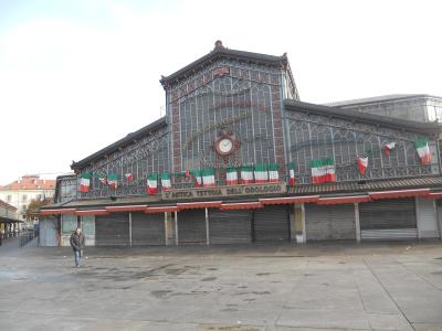 The image shows the "L'antica tettoia dell'orologio" (The old clock canopy), a historic iron-and-glass market hall in Turin, Italy, decorated with Italian flags and signage referencing the 150th anniversary of Italian unification.