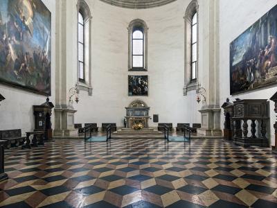 The image shows the interior of a chapel with a distinctive black, white, and tan checkered floor, large Baroque-style paintings on the walls, wooden confessionals, and an altar at the far end under a dome.