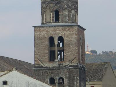 A tall, historic brick bell tower (campanile) with arched openings and a domed top, set against a cloudy sky with surrounding rooftops and distant hills.