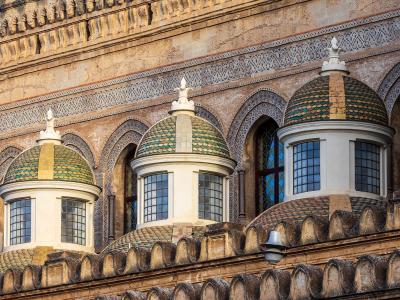A close-up architectural detail showing three small domed lanterns with green and yellow glazed tiles, set against a stone facade featuring Moorish-style horseshoe arches and intricate geometric tilework.