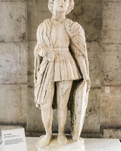 A marble statue of a standing male figure (San Liberale) displayed indoors against a stone wall, with an informational placard identifying it as "San Liberale" from the "Musei Civici di Treviso".