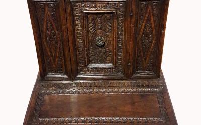 A dark wooden Renaissance-style prayer desk (or prie-dieu) with carved panels, a central door with a metal knob, and an attached kneeler, photographed against a plain white background.