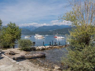 A view from a pebbly shoreline with small wooden docks and boats on a lake, framed by trees, with mountains in the background under a partly cloudy sky.