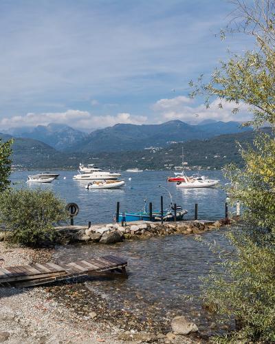 A view from a pebbly shoreline with small wooden docks and boats on a lake, framed by trees, with mountains in the background under a partly cloudy sky.