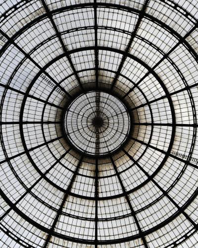 A low-angle view looking directly up at a large, circular iron-and-glass dome with a radial grid pattern and decorative side arches.