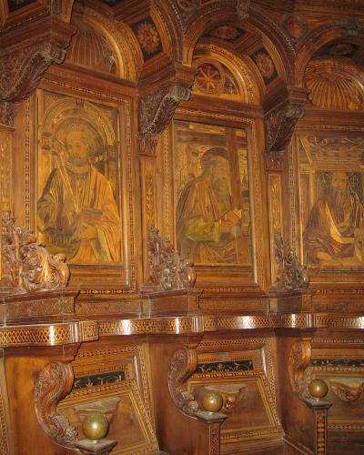 The image shows an ornate, gilded wooden choir stall (coro) featuring painted panels of saints and intricate marquetry, with identifying text "Coro rinascimentale, Certosa di Pavia, Lombardia" in the filename.