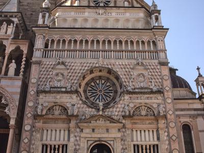 The image shows the ornate Renaissance facade of a chapel with a distinctive diamond-patterned marble exterior, a large central rose window, and a dome, situated next to a larger basilica structure under a clear blue sky.