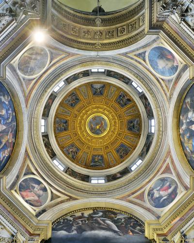 A low-angle interior view of an ornate, gilded dome ceiling with frescoes, marble columns, and inscriptions on the piers, identified by the filename as the Cappella Chigi in Santa Maria del Popolo, Rome.
