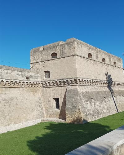 The image shows the massive stone ramparts and bastions of a medieval fortress, specifically the Castello Svevo in Bari, Italy, characterized by its thick defensive walls, crenellations, and a palm tree in the foreground.