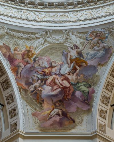 The image shows the interior ceiling of a church dome featuring a Baroque-style fresco of religious figures surrounded by stucco decorations and architectural moldings.