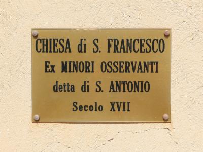 A brass plaque mounted on a textured beige wall, reading "CHIESA di S. FRANCESCO / Ex MINORI OSSERVANTI / detta di S. ANTONIO / Secolo XVII".
