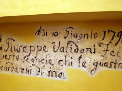 The image shows a close-up of an old, handwritten inscription on a yellow-painted wall, with text reading "Di 10 Giugno 1793 / Giuseppe Validoni Feci / queste scancie chi le guasta / ricordatevi di me." (On June 10, 1793 / Giuseppe Validoni made /