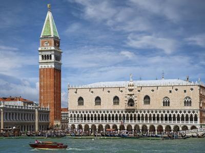 The image shows the Doge’s Palace (Palazzo Ducale) and St. Mark’s Campanile in Venice, Italy, viewed from the water with boats and gondolas in the foreground under a partly cloudy sky.