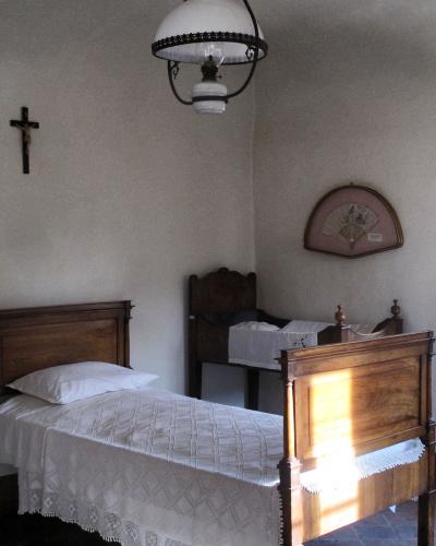 The image shows a sparsely furnished bedroom interior with two wooden beds, a hanging oil lamp, a crucifix on the wall, and a decorative fan, consistent with a historical museum room.