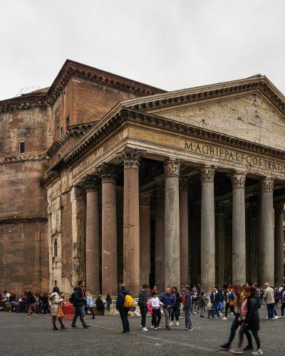 The image shows the exterior of the Pantheon in Rome, featuring its iconic portico with Corinthian columns, pediment, and cylindrical brick drum, with crowds of tourists in the foreground.