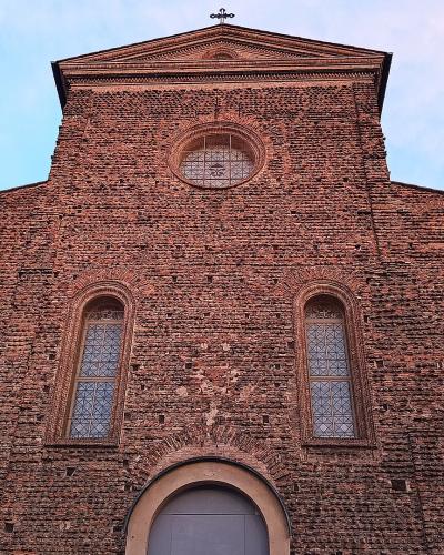 A low-angle photograph of a large, red-brick church facade featuring a central pediment topped with a cross, a circular window, two tall arched windows, and smaller circular windows on the sides.
