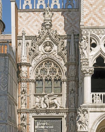 The image shows the ornate Gothic facade of the Porta della Carta, the main entrance to the Doge's Palace in Venice, featuring a large winged lion statue and a poster for a Henri Rousseau exhibition.