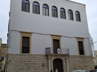 A white, multi-story building with a stone base and arched windows on the upper floor, featuring a sign that reads "MUSEO DIOCESANO" above an entrance balcony.