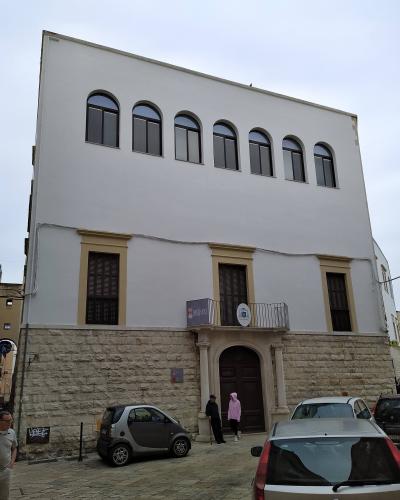 A white, multi-story building with a stone base and arched windows on the upper floor, featuring a sign that reads "MUSEO DIOCESANO" above an entrance balcony.