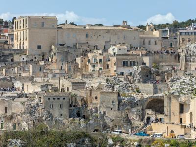 A panoramic view of the Sassi di Matera, showing the distinctive cave dwellings and stone buildings built into the ravine, with the large Palazzo Lanfranchi visible as the prominent rectangular building on the upper left.