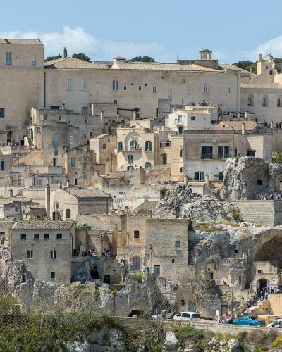 A panoramic view of the Sassi di Matera, showing the distinctive cave dwellings and stone buildings built into the ravine, with the large Palazzo Lanfranchi visible as the prominent rectangular building on the upper left.