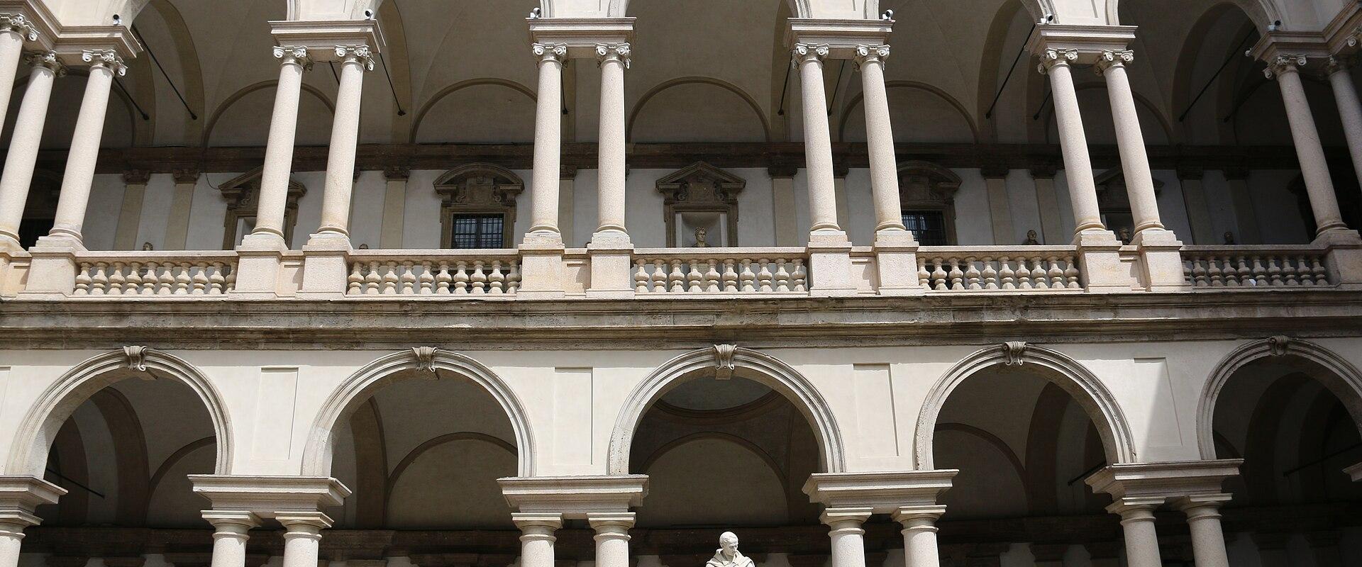 A two-story Renaissance-style courtyard with arched loggias supported by columns, featuring a central statue of a robed figure on a pedestal under the lower arches.