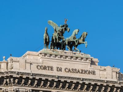 The image shows the roofline and pediment of a grand neoclassical building featuring a bronze quadriga sculpture and the inscription "CORTE DI CASSAZIONE" in large capital letters.
