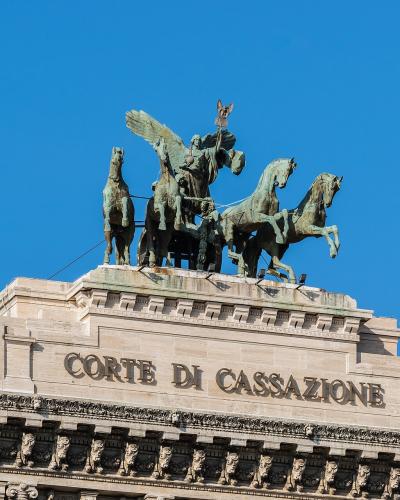 The image shows the roofline and pediment of a grand neoclassical building featuring a bronze quadriga sculpture and the inscription "CORTE DI CASSAZIONE" in large capital letters.