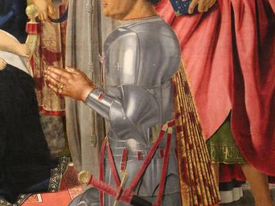 A close-up detail of a Renaissance painting showing a man in full plate armor kneeling in prayer, with a helmet and sword on the ground before him, surrounded by other figures in religious vestments.