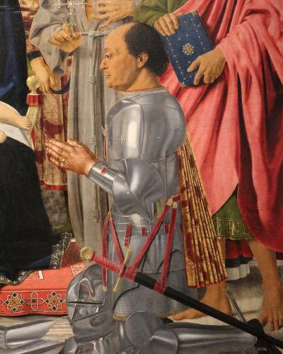 A close-up detail of a Renaissance painting showing a man in full plate armor kneeling in prayer, with a helmet and sword on the ground before him, surrounded by other figures in religious vestments.
