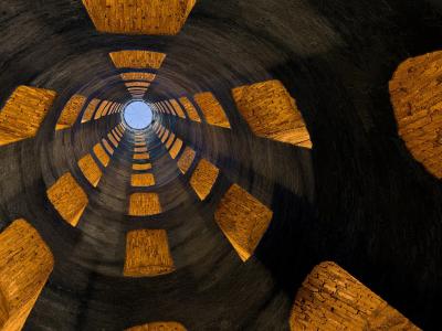 A view looking straight up the interior of a deep, cylindrical stone well with a double-helix ramp structure and a circular opening to the sky at the top.