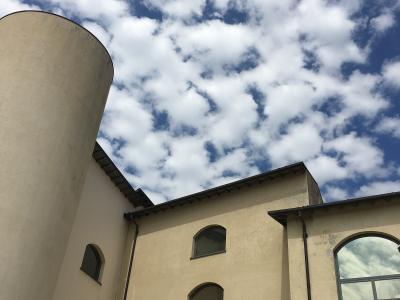 A low-angle view of a beige building with arched windows and a cylindrical tower against a cloudy blue sky.