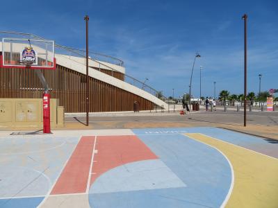 The image shows an outdoor basketball court with colorful painted surfaces, a Red Bull-branded hoop, and a modern wooden-and-concrete structure in the background; the word “RIMINI” is painted on the court surface.