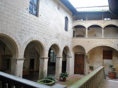 The image shows the interior courtyard of a historic stone building featuring arched loggias, a central fountain, and Renaissance-style architectural details.