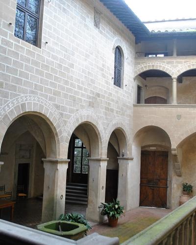 The image shows the interior courtyard of a historic stone building featuring arched loggias, a central fountain, and Renaissance-style architectural details.