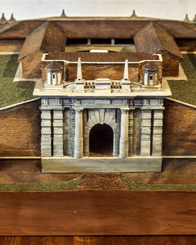 A detailed scale model of a fortified star-shaped city with a prominent arched gate (Porta Udine) and surrounding ramparts, displayed indoors on a wooden base.