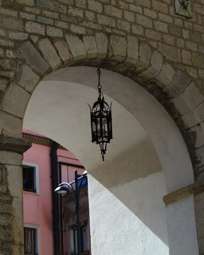 A close-up of a stone archway with a white plastered interior, featuring a hanging black metal lantern and a pink building visible through the opening.