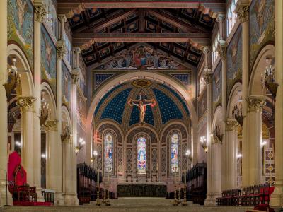 The interior of a grand cathedral featuring ornate columns, colorful frescoes, a large crucifix, and stained glass windows.
